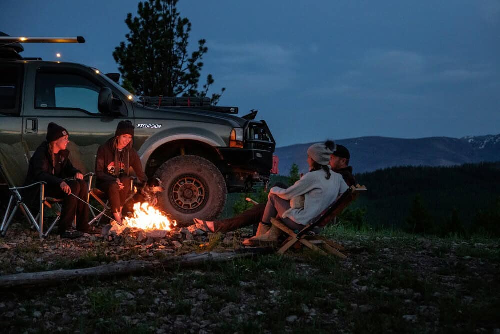 people sitting around campfire beside campervan