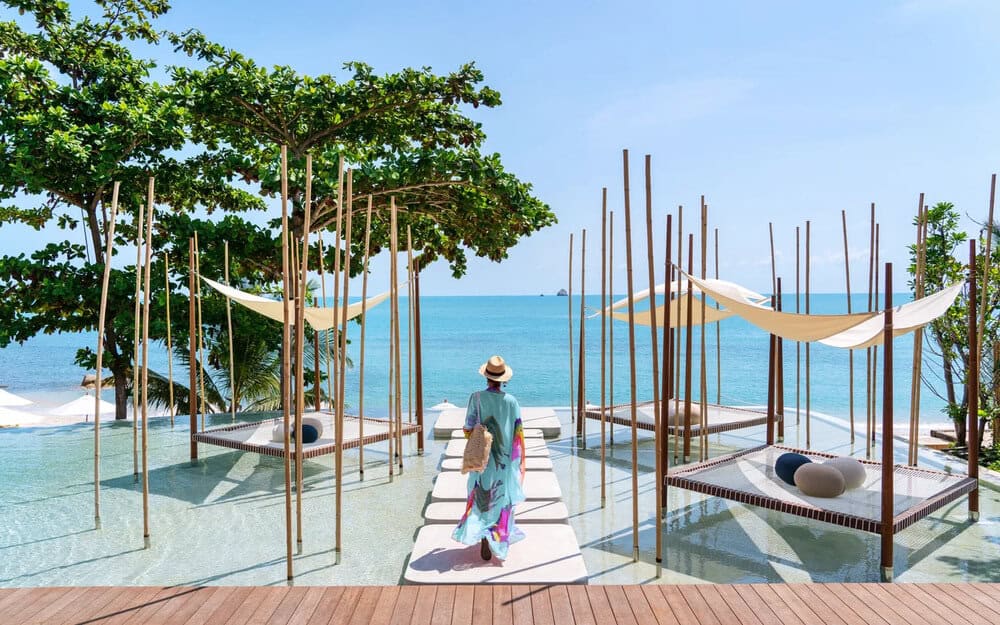 woman walking on boardwalk above pool in front of ocean six senses koh samui