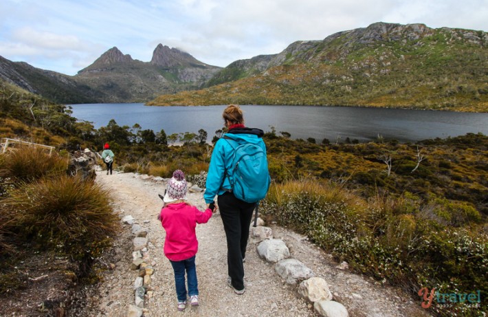 a woman and a child holding hands while walking next to a lake