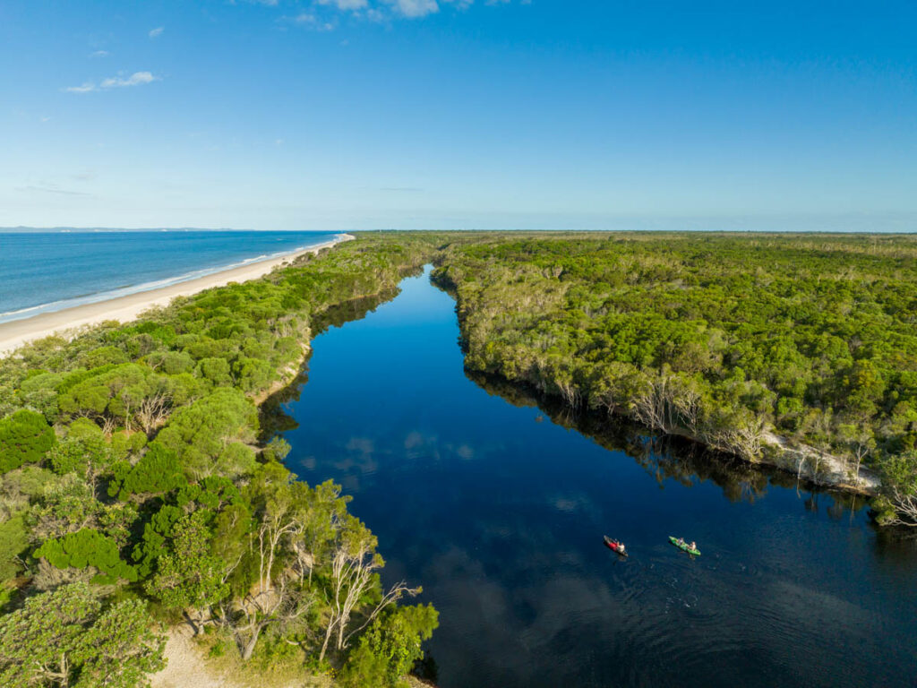 people kayaking on river parallel to beach on bribie island