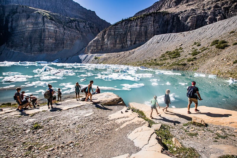 people standing on edge of Grinnell Lake with icebergs in it 