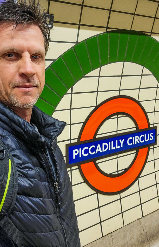 man taking selfie in front of piccadilly tube sign