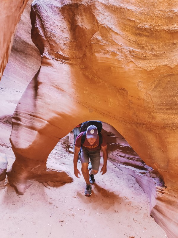 man crouching under low arch in Peek a Boo Canyon