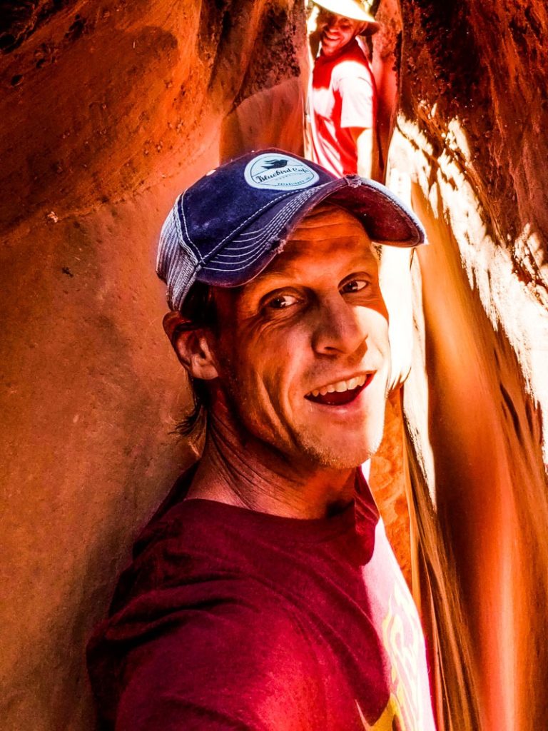 man walking sideways through narrow spooky slot canyon