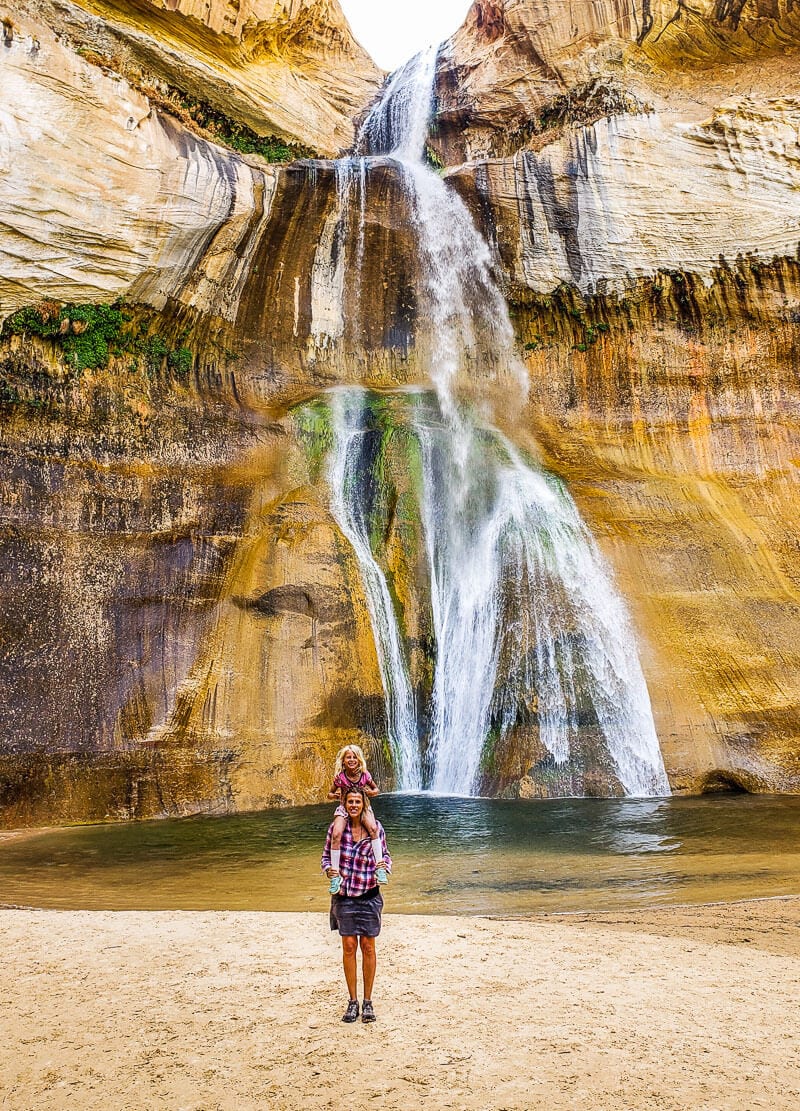 woman with child on shoulders posing in front of Lower Creek Calf Falls, Escalante