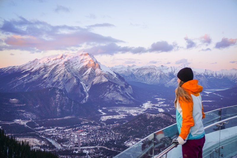 person sanding on edge of lookout looking at Banff and snow capped Sulphur Mountain 