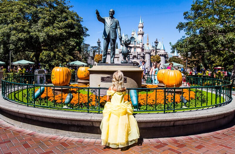 girl in a princess dress looking at a mickey mouse statue