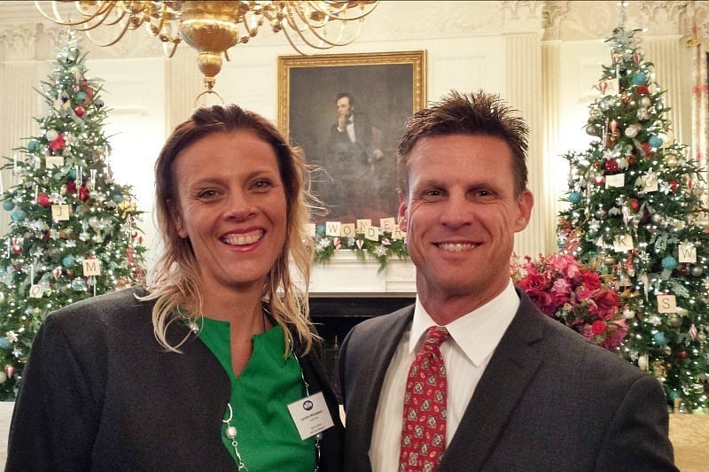 man and woman posing in front of christmas trees and abe lincoln portrait inside the white house