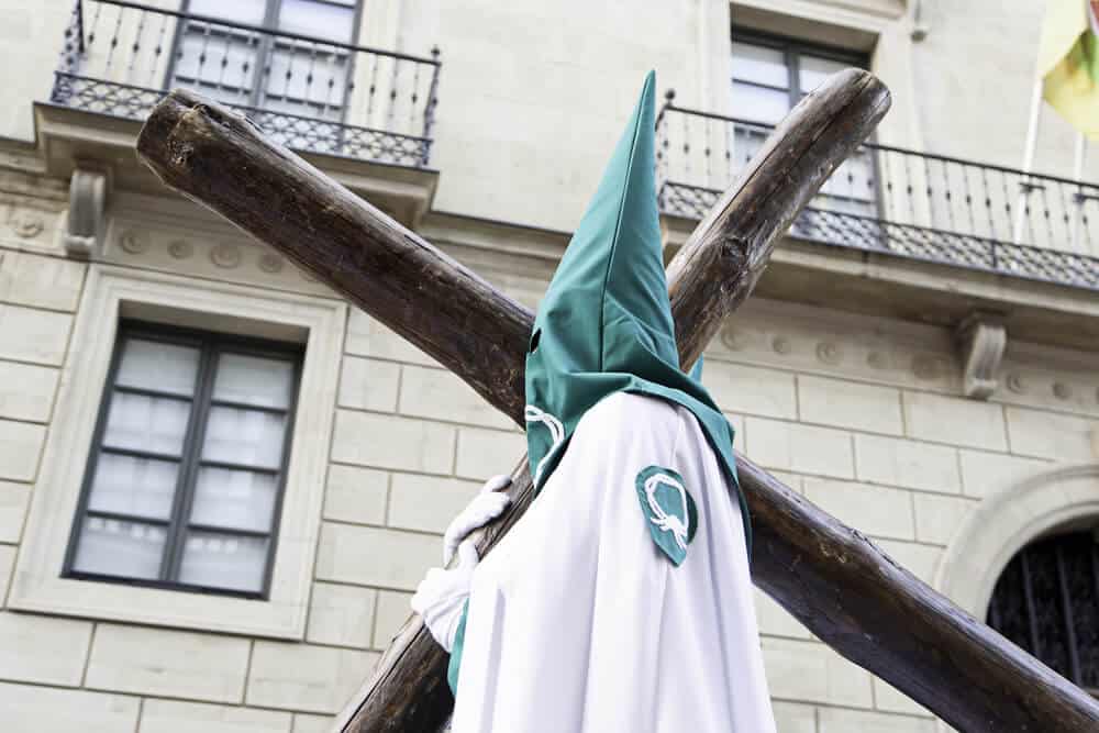 man with green hood carrying cross