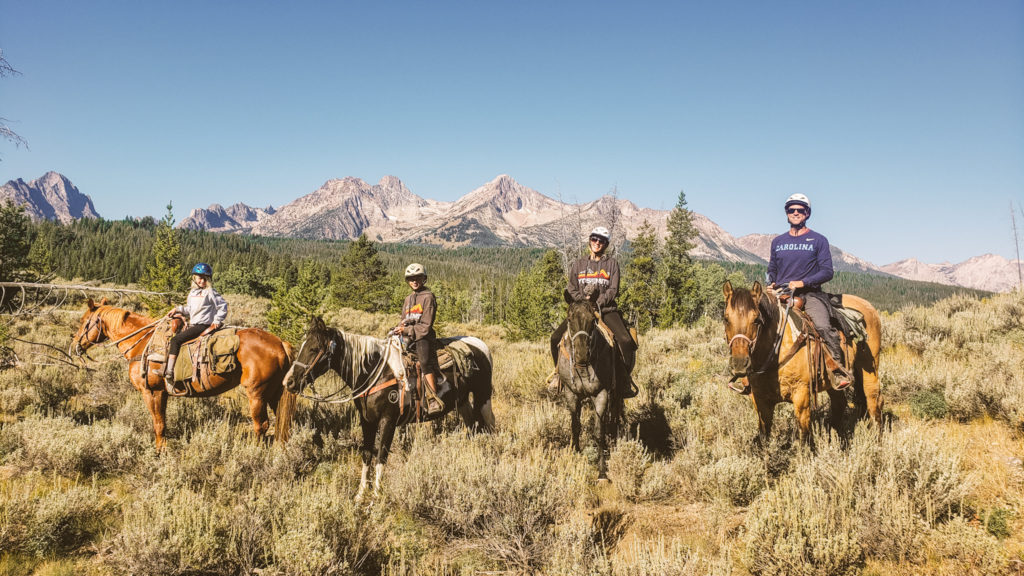 family on horseeback posing with sawtooh mountains behind them  