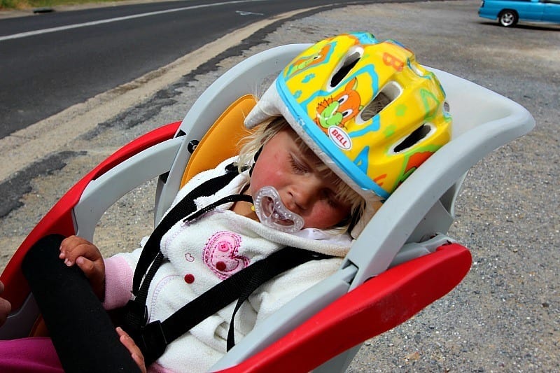 A child wearing a helmet asleep in bike carrier