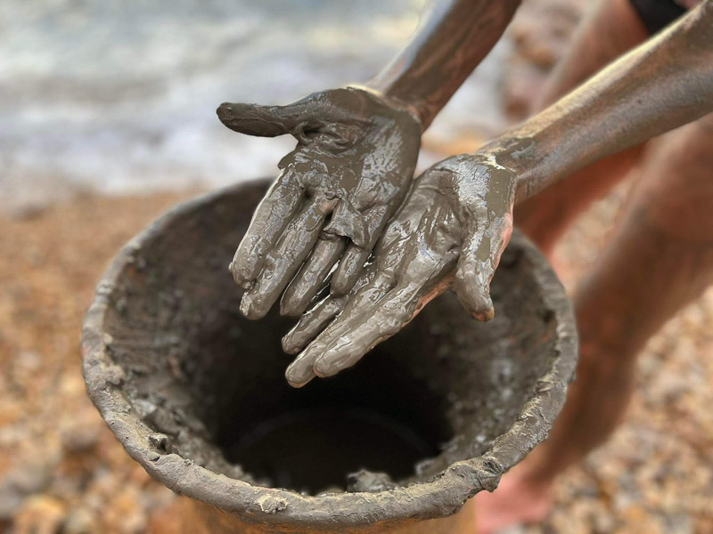 hands covered in mud over urn