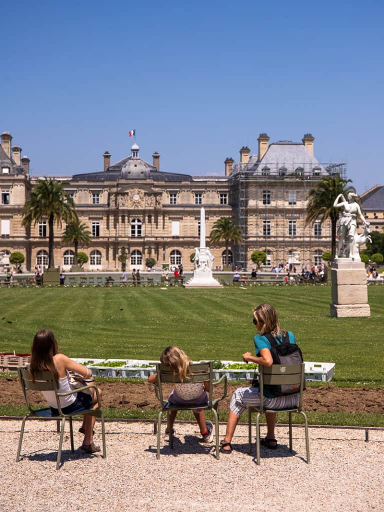 caz and girls sitting on chairs looking at palace in luxembourg gardens