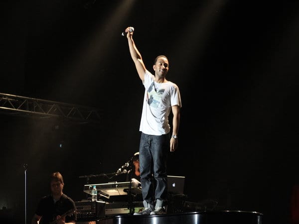 JOHN LEGEND standing on stage holding up a microphone