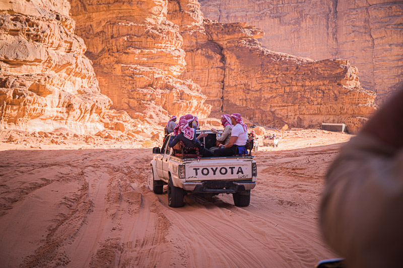 group of people sitting in the back of a pickup driving through Wadi Rum